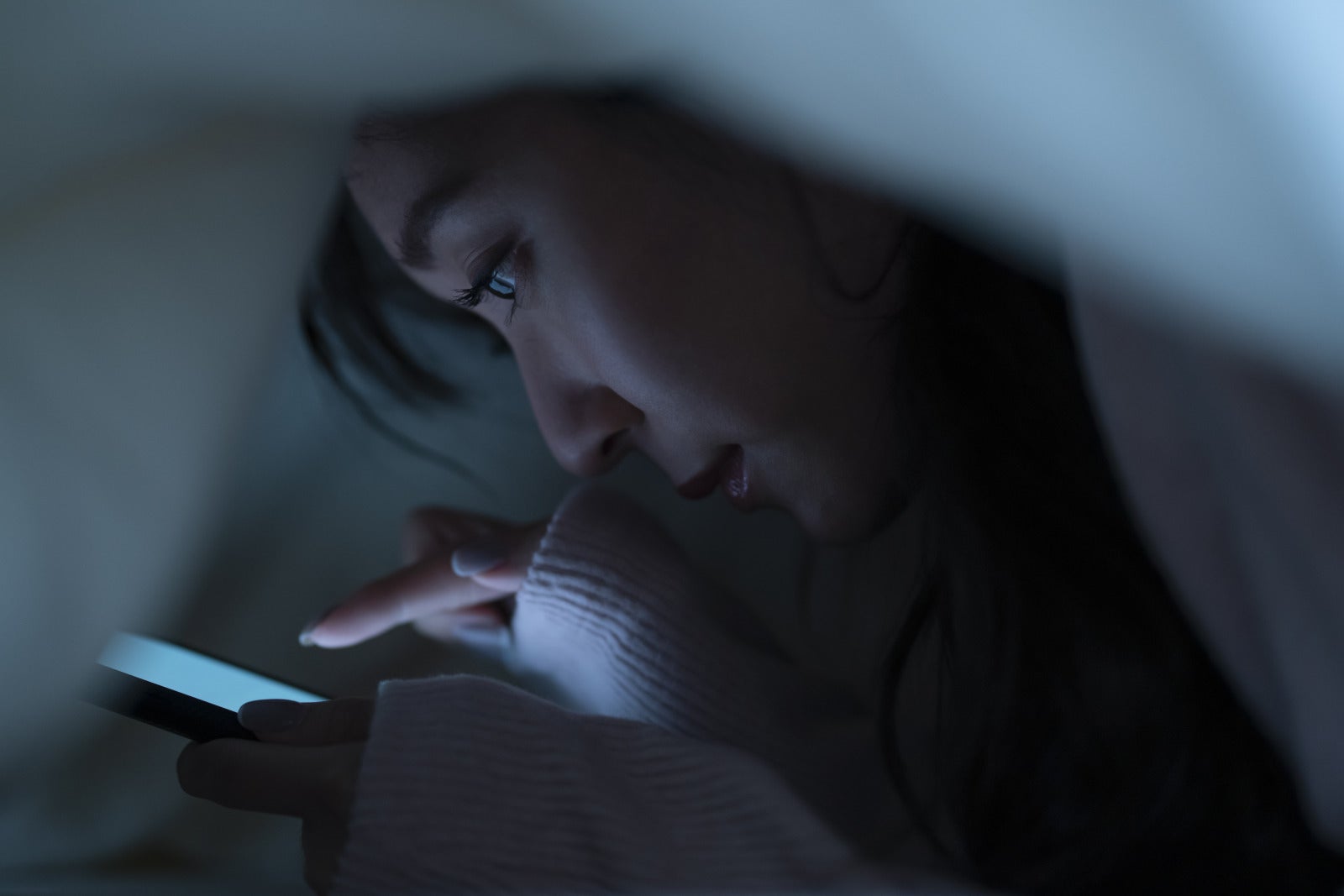 Woman playing phone games night on bed dark