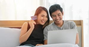 asian couple shopping online and paying with credit card at laptop computer happy couple at home surfing the net in bed photo