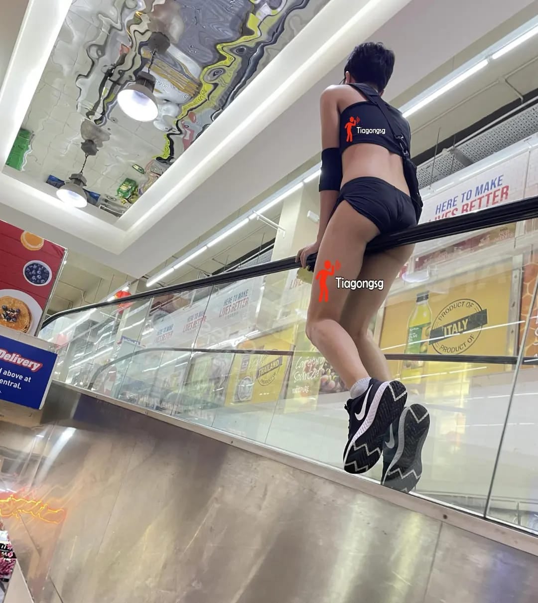 man rides escalator singapore wearing shorts and crop top