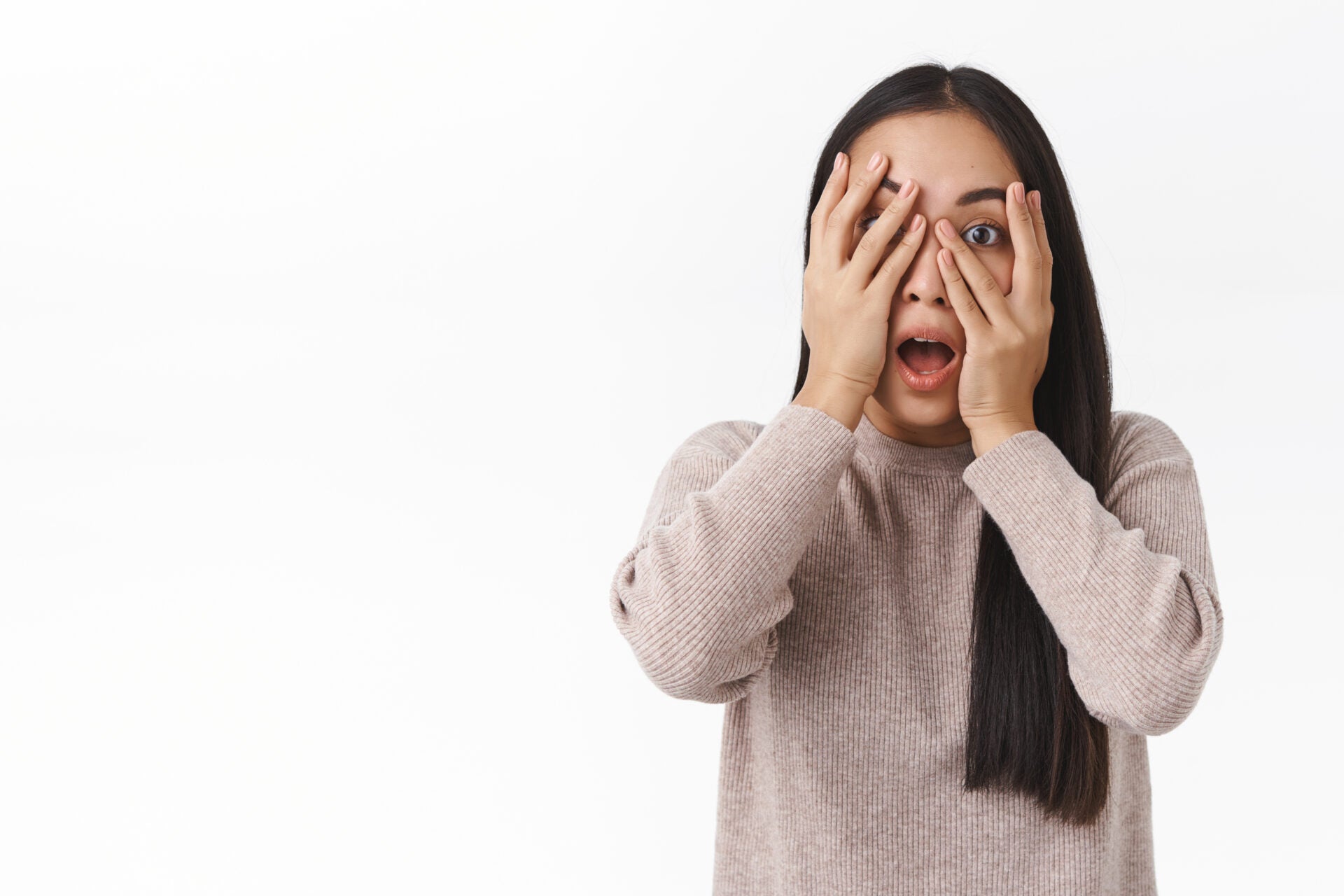scared embarrassed cute asian girl hiding face hold hands eyes peeking camera frightened alarmed watching horror movie alone dark afraid clowns standing white background shook