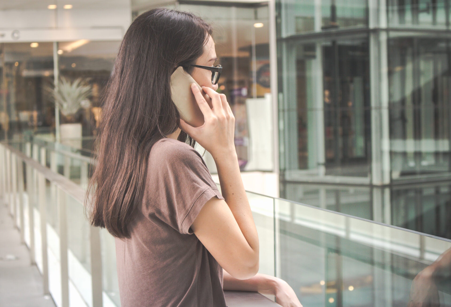 Woman Talking Mobile Phone While Standing By Railing Shopping Mall