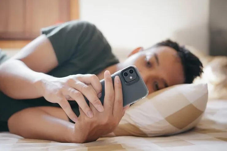 Young Man Lying Bed Looking His Smartphone With Thoughtful Expression Relaxed Cozy Bedroom 885751 513